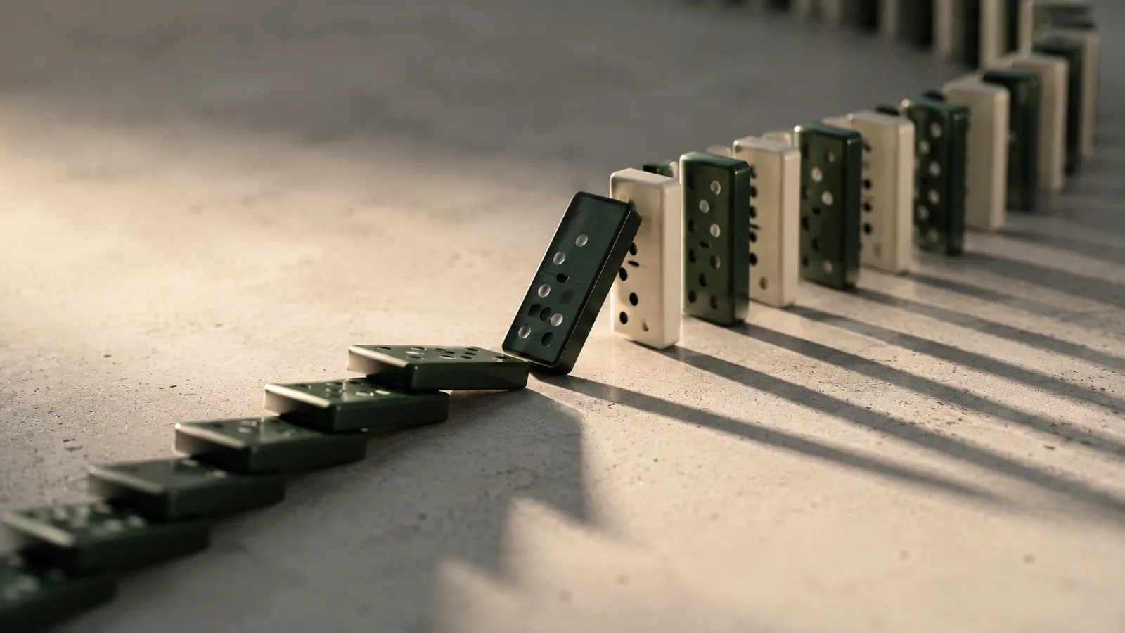 A line of dominoes on concrete where the chain has toppled up to a point and stopped, one fallen tile leaning against the next, with the rest of the row still standing upright into the distance.