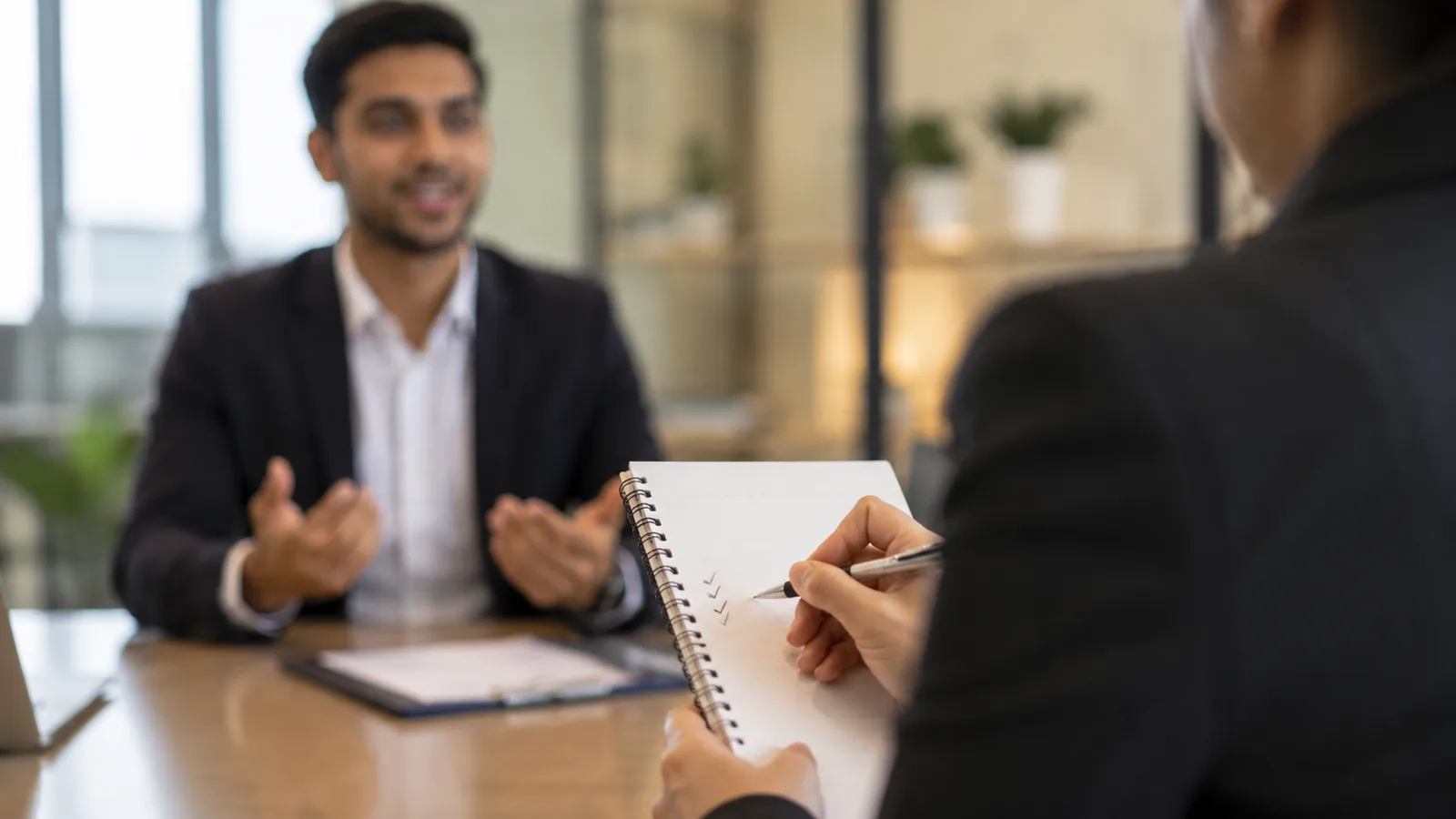 An interviewer writing small checkmarks on a notepad while a candidate answers confidently, illustrating a strong answer to the AI question