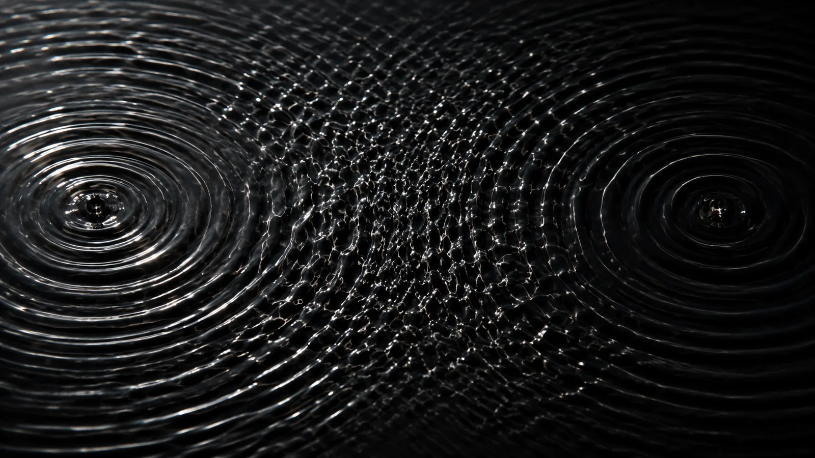 Two sets of circular ripples spreading across dark water from separate points, meeting in the middle of the frame where the pattern breaks into disordered chop.